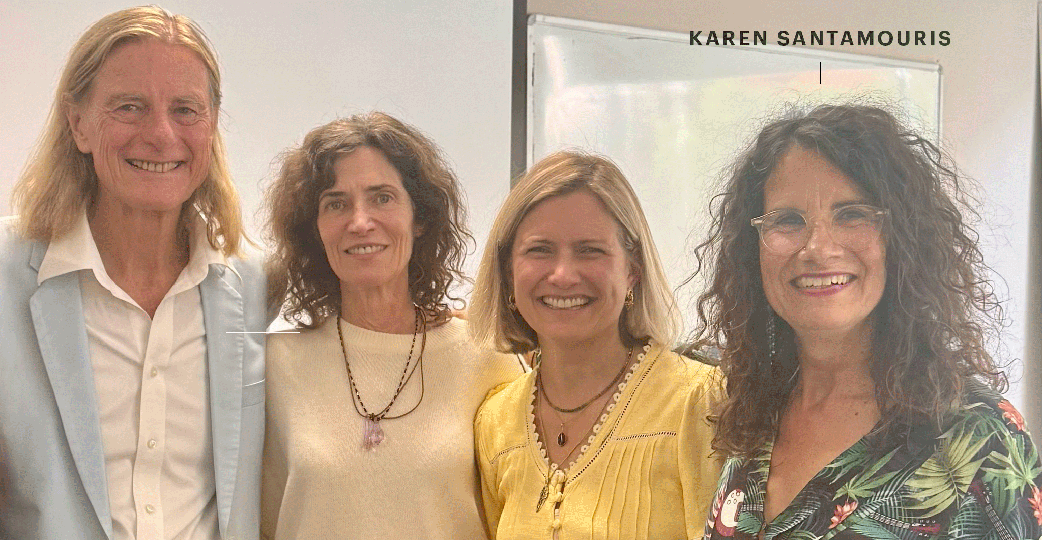 Vier lächelnde Personen stehen eng nebeneinander in einem hellen Raum vor einer Tafel