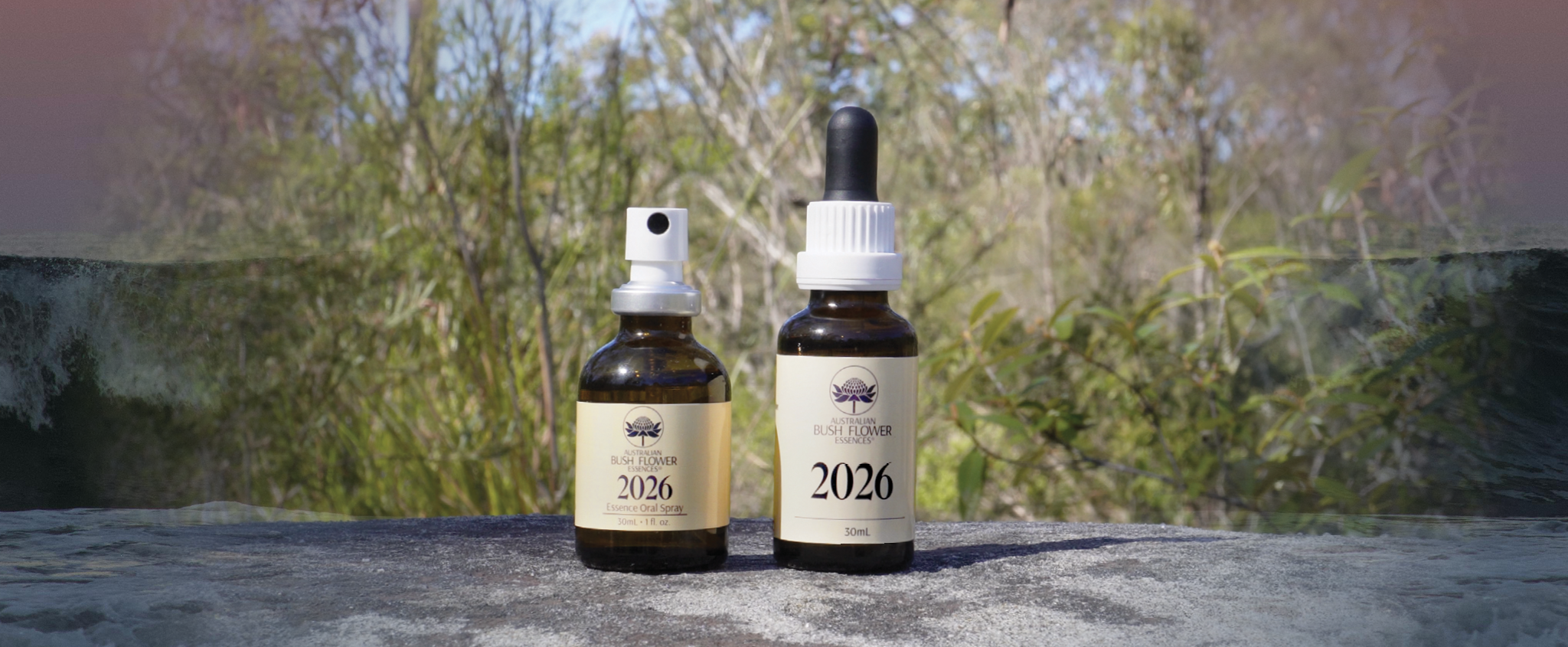 Zwei Fläschchen der Australian Bush Flower Essences 2026 Essence vor australischem Buschland.